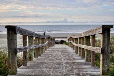 The boardwalk at the back of the property, looking along weathered timber decking between handrails to the beach and the sea beyond. The boards are dry and even, with no lifted nails or soft sections.